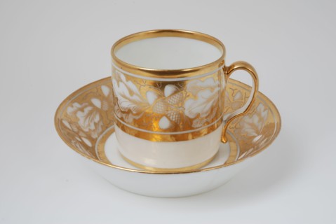 White cup and saucer with gold colored band with acorn and leaf decoration, cup and saucer drinking utensils tableware holder