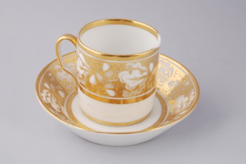 White cup and saucer with gold colored band with acorn and leaf decoration, cup and saucer drinking utensils tableware holder