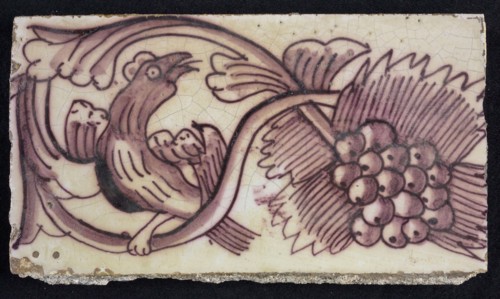 Rectangular edge tile in purple with serpentine decor of leafy tendril, toasted bird to the right, grape bunch, edge tile wall