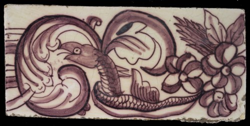 Rectangular edge tile in purple with swirling design of leaves, flowers and twisted snake with scales and fin, border tile wall