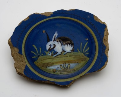 Fragment majolica pancake plate with rabbit or hare on dark blue background, plate crockery holder soil find ceramic earthenware