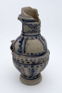 Stoneware jug with kerf-cut decor on shoulder, round neck band with three medallions in which mask, jug crockery holder soil
