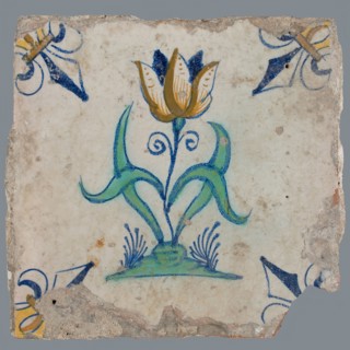 Tile, flower on ground in orange, brown, yellow, green and blue on white, corner pattern french lily, corner point yellow, wall