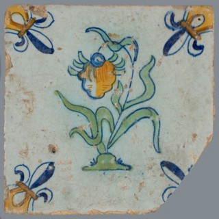 Tile, flower on ground in orange, yellow, green and blue on white, corner pattern french lily, corner point yellow, wall tile