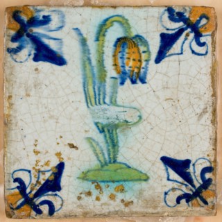 Tile, flower on ground in orange, green and blue on white, corner pattern french lily, corner point orange, on shelf in wax