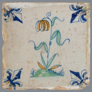 Tile, flower on ground in orange, green and blue on white, corner pattern french lily, corner point orange, wall tile