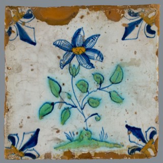 Tile, flower on ground in orange, green and blue on white, corner pattern french lily, corner point orange, wall tile