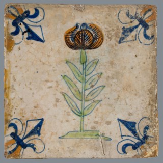 Tile, flower on ground in orange, green and blue on white, corner pattern french lily, corner point orange, wall tile