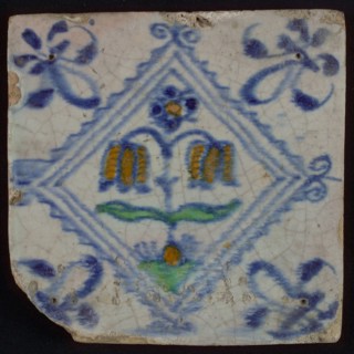 Tile, double flower on ground in orange, green and blue on white, inside serrated square with plume, corner pattern french lily