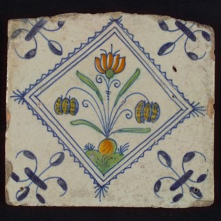 Tile, double flower on ground in orange, green and blue on white, inside serrated square with plume, corner pattern french lily