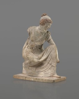 Terracotta figurine of a girl throwing dice. Female figurine of a crouching girl throwing dice;