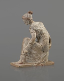 Terracotta figurine of a girl throwing dice. Female figurine in a long, finely pleated sleeveless