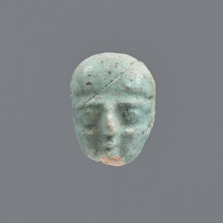 Fragment of a shabti, grave goods, wigs. Face of a shabti figurine with carefully rendered facial