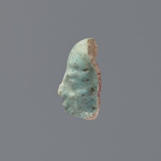 Fragment of a shabti, grave goods, wigs. Face of a shabti figurine with carefully rendered facial