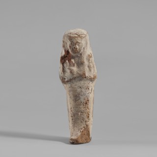 Ushabti. Mummy-shaped figurine made of clay, painted cream with black details. Arms crossed on the