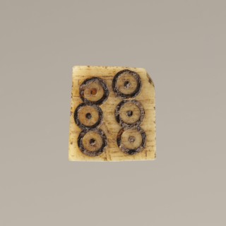 Game die made of animal bone with six unequal sides. Each side is engraved with a number from 1 to