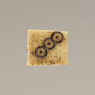 Game die made of animal bone with six unequal sides. Each side is engraved with a number from 1 to