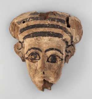 Sarcophagus mask with an elongated, triangular face. A fragment of a wig is preserved above the