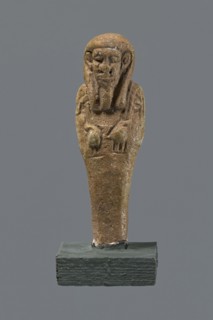 Shabti, mummy-shaped figurine standing on a base, back supported by a pillar/pilaster. Arms crossed