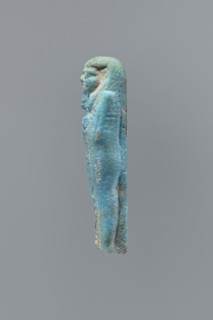 Ushabti, mummy-shaped figurine, back supported on a flat pillar. Feet missing. Arms crossed on the