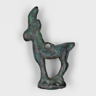 Figurine of an ibex goat standing on a hollow prism base with two pairs of holes on the longer