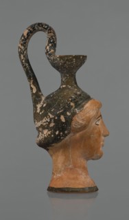 Oinochoe in the shape of a woman's head. Yellowish clay with orange surface and areas of shiny
