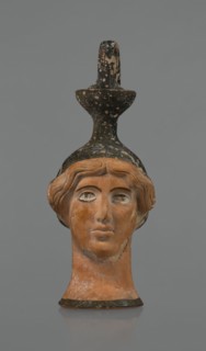 Oinochoe in the shape of a woman's head. Yellowish clay with orange surface, in places shiny black