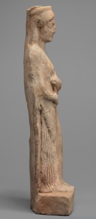 Figurine of a woman standing on a rectangular base. The woman is dressed in a finely pleated chiton