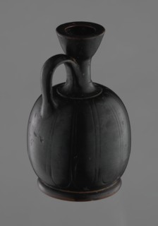 Black-finished aryballoid lekythos coated with black varnish. The medium, flat foot flows directly