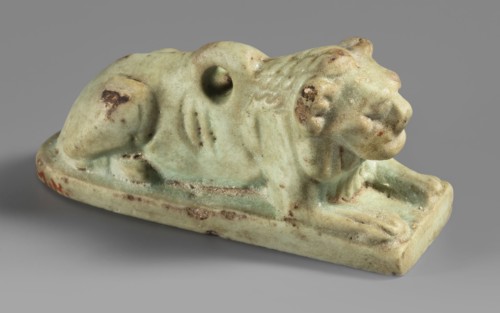 Amulet in the shape of a lion lying on a flat base, with paws stretched forward, head facing