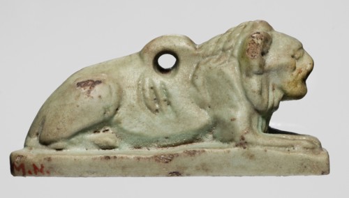 Amulet in the shape of a lion lying on a flat base, with paws stretched forward, head facing