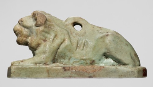 Amulet in the shape of a lion lying on a flat base, with paws stretched forward, head facing