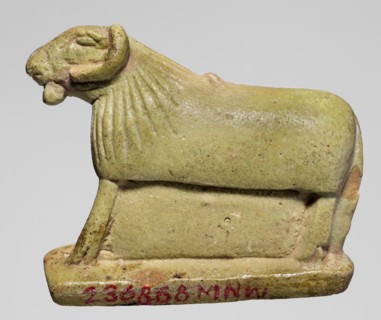 Amulet in the shape of a ram standing on a stand with curled horns and a short beard. The fur