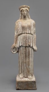 Female terracotta figurine of a standing woman positioned frontally on a quadrangular base. The