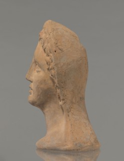 Votive female head, Female head wearing a wreath, from under which lush locks of hair curl down the