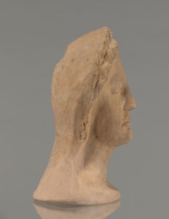 Votive female head, Female head wearing a wreath, from under which lush locks of hair curl down the