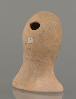 Votive female head, female head wearing a wreath, from under which lush locks of hair curl down the