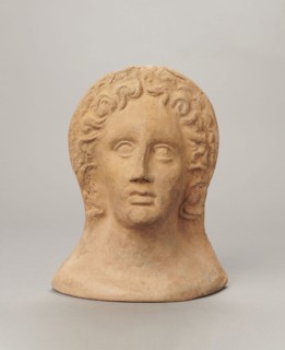 Votive female head. Female head wearing a wreath, from under which lush locks of hair curl down the