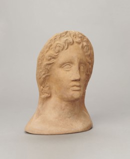 Votive female head, Female head wearing a wreath, from under which lush locks of hair curl down the