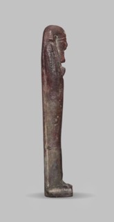 Ushabti, A shabti figurine dressed in a shroud stands on a base. On the head is a smooth wig,