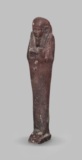 Ushabti, A shabti figurine dressed in a shroud stands on a base. On the head is a smooth wig,
