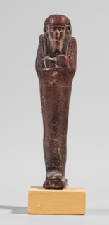 Ushabti, A shabti figurine dressed in a shroud stands on a base. On the head is a smooth wig,