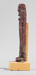 Ushabti, A shabti figurine dressed in a shroud stands on a base. On the head is a smooth wig,
