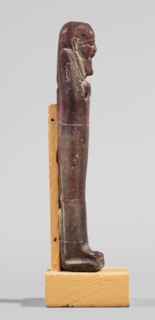 Ushabti, A shabti figurine dressed in a shroud stands on a base. On the head is a smooth wig,