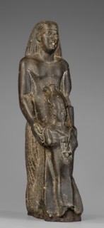 Figurine of a priest holding a statuette of the god Osiris. The priest stands, holding the