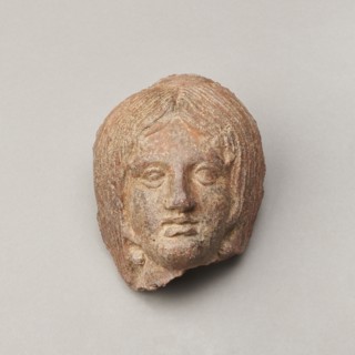 Female votive head, Female head with long, straight hair falling to the shoulders. Neck partially