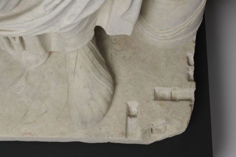 Figure of a striding man dressed in a tunic and toga. The folds of the toga flow widely, with a