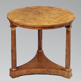Round table on three legs in the form of slender columns with smooth shafts, mounted on a