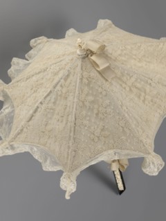 Women's umbrella made of white lace. Its canopy is trimmed with cream silk at the bottom, which