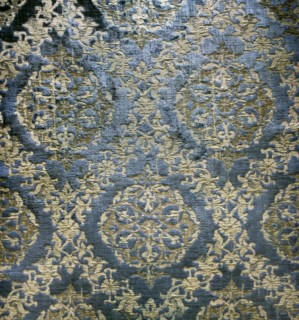 A fabric fragment: a diagonal net of plant and floral tendrils against a blue velvet background. In